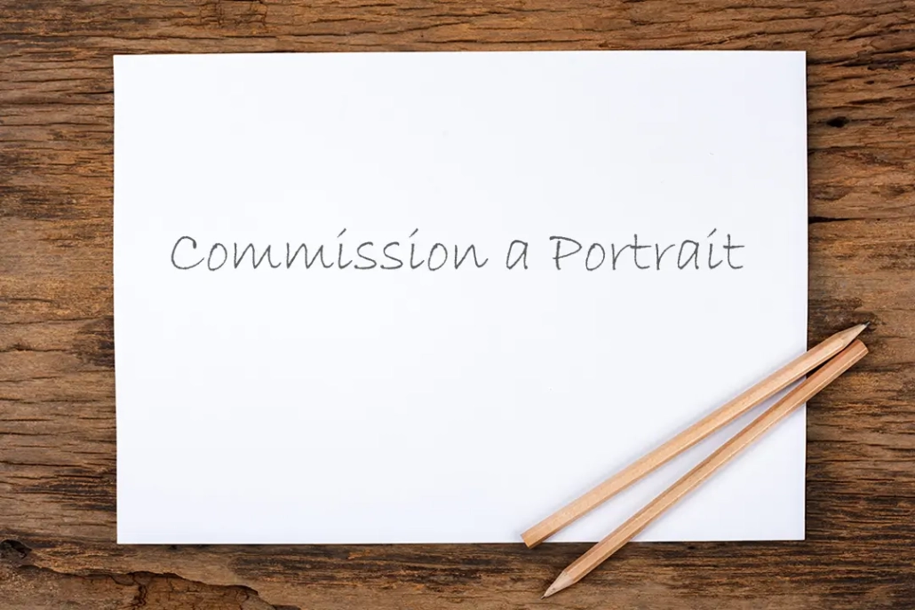 Drawing paper with “Commission a Portrait” written in pencil beside a pair of pencils